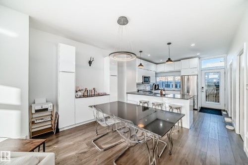 Open-concept kitchen and dining area featuring wood-finish flooring, white cabinetry, stainless steel appliances, a kitchen island with seating, and recessed lighting - 14812 98 Avenue, Edmonton, AB - Indoor