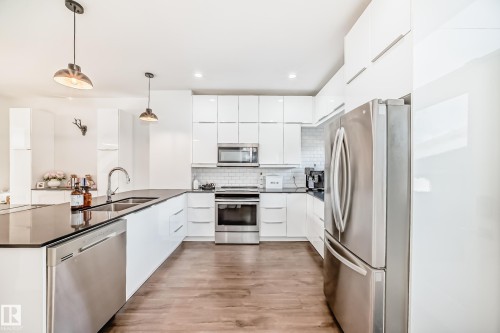 Modern kitchen featuring white flat-panel cabinetry, a stainless steel appliance suite, black countertops, and a subway tile backsplash - 14812 98 Avenue, Edmonton, AB - Indoor Photo Showing Kitchen With Stainless Steel Kitchen With Double Sink With Upgraded Kitchen