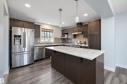Kitchen featuring wood-finish flooring, dark cabinetry, light countertops, stainless steel appliances, and a hexagonal tile backsplash - 