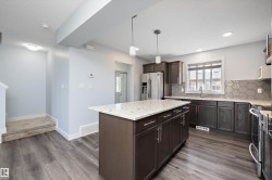 Kitchen featuring a central island with a light-toned countertop, dark wood-finish cabinetry, stainless steel appliances, and a hexagon tile backsplash - 