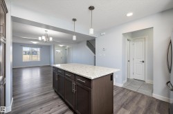 Kitchen island featuring a light-toned countertop, pendant lighting, dark wood-finish cabinetry, and stainless steel hardware - 