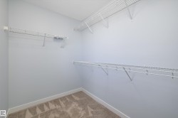 Walk-in closet featuring light gray walls, white baseboards, and patterned carpeting - 