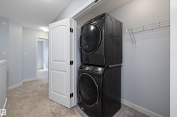 Dedicated laundry area featuring a stacked washer and dryer, tile flooring, and wall-mounted wire shelving - 