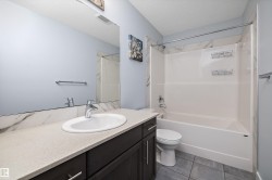 Bathroom featuring a dark wood-finish vanity with a light-toned countertop, a full-width mirror, and a white integrated sink - 