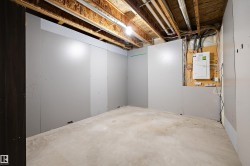 Unfinished basement space with concrete flooring, partial drywall installation, exposed ceiling joists, and visible utility systems - 