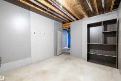 Unfinished lower level featuring exposed ceiling joists, concrete flooring, partially drywalled walls, an open doorway, and a built-in shelving unit - 