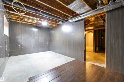 Unfinished room featuring exposed ceiling joists, concrete flooring, partial dark wood-finish wall paneling, and an exposed ventilation duct system - 