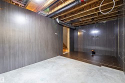Partially finished basement space featuring panel walls, exposed ceiling joists, existing ductwork, concrete flooring, and partial wood-finish flooring installation - 