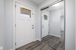 Entryway featuring a white paneled door with window, wood-finish flooring, and mirrored sliding closet doors - 
