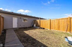 Private backyard space featuring tall wood fencing, a grey siding exterior, a white exterior door, and a single window with white trim - 