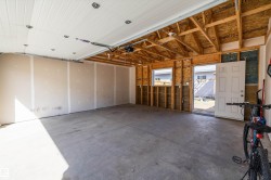 Spacious garage featuring concrete flooring, an overhead garage door, exposed ceiling rafters, and a side access door - 