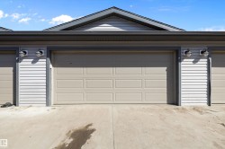 Exterior featuring light beige paneled garage doors, white horizontal siding, dark grey trim, and a concrete driveway - 