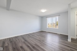Spacious room featuring light gray walls, wood-finish flooring, a contemporary flush mount light fixture, and a large window with white trim - 