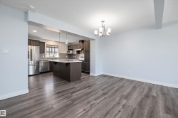 Open-concept kitchen and dining area featuring wood-finish flooring, dark wood cabinetry, stainless steel appliances, and a central kitchen island with a light-colored countertop - 