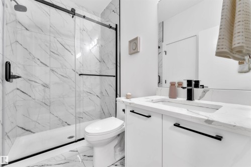 Modern bathroom featuring large-format marble-look tile, a glass-enclosed shower with black fixtures, and a white vanity with a rectangular undermount sink - 1809 18A Avenue, Edmonton, AB - Indoor Photo Showing Bathroom