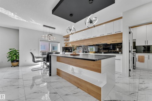 Modern kitchen featuring a large central island with a contrasting dark countertop, white and wood-finish cabinetry, sleek black backsplash, and contemporary pendant lighting - 1809 18A Avenue, Edmonton, AB - Indoor Photo Showing Kitchen