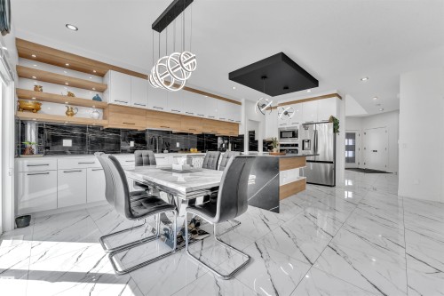 Modern kitchen featuring a large central island with a waterfall countertop, integrated stainless steel appliances, and sleek white cabinetry with wood-finish accents - 1809 18A Avenue, Edmonton, AB - Indoor Photo Showing Dining Room