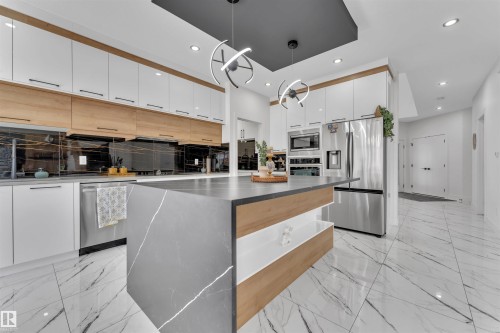Kitchen featuring a waterfall island with a stone-finish countertop, stainless steel appliances, two-tone cabinetry with wood-finish accents, and marble-look tile flooring - 1809 18A Avenue, Edmonton, AB - Indoor Photo Showing Kitchen With Upgraded Kitchen