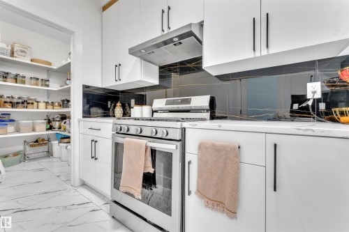 Modern kitchen featuring white cabinetry, a stainless steel range, and a black and gold veined backsplash - 1809 18A Avenue, Edmonton, AB - Indoor Photo Showing Kitchen