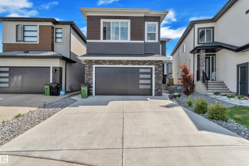 Contemporary exterior featuring a concrete driveway, attached two-car garage with frosted pane windows, and stone veneer accents - 1809 18A Avenue, Edmonton, AB - Outdoor With Facade