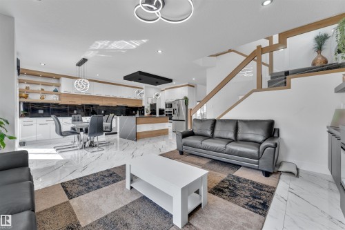 Open-concept living space featuring high-gloss tile flooring, a modern staircase with wood and glass railings, contemporary overhead lighting, and a kitchen with white cabinetry, wood-finish shelving, and built-in appliances - 1809 18A Avenue, Edmonton, AB - Indoor Photo Showing Living Room