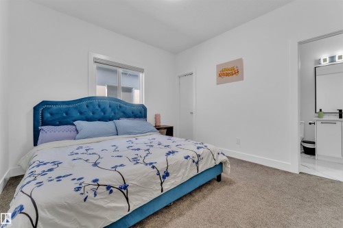 Carpeted bedroom featuring a window, white baseboards, and a doorway opening to a bathroom with tile flooring, a single vanity, and a mirror with integrated lighting - 1809 18A Avenue, Edmonton, AB - Indoor Photo Showing Bedroom