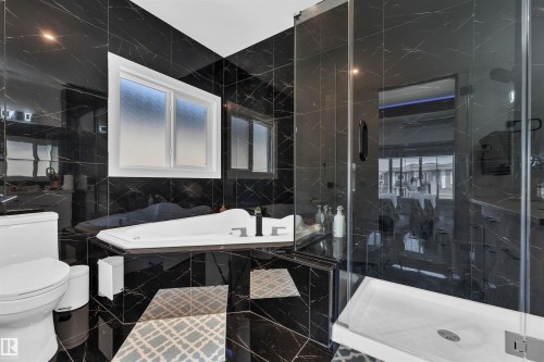 Sleek bathroom featuring black marbled tile walls and flooring, a built-in soaking tub with black fixtures, a glass-enclosed shower, and a privacy window - 1809 18A Avenue, Edmonton, AB - Indoor Photo Showing Bathroom