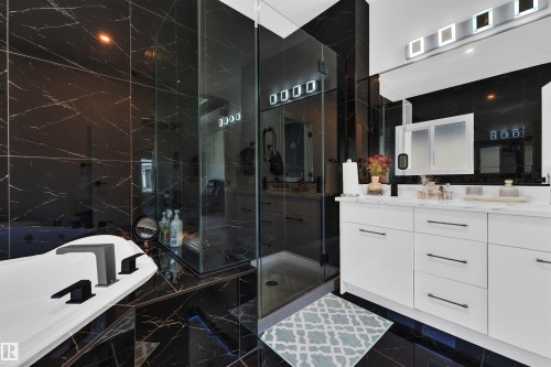 Full bathroom featuring black marble-style tile flooring and walls, a glass-enclosed shower, a white soaking tub with matte black fixtures, a double vanity with white cabinetry, and a mirrored medicine cabinet - 1809 18A Avenue, Edmonton, AB - Indoor Photo Showing Bathroom