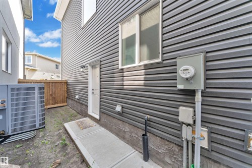 Side exterior featuring horizontal panel siding, a white entry door with an overhead light fixture, and a concrete walkway - 1809 18A Avenue, Edmonton, AB - Outdoor With Exterior