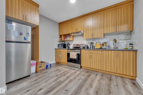 Kitchen featuring wood-finish cabinetry, stainless steel appliances, gray countertops, a marble-look backsplash, and wood-finish flooring - 1809 18A Avenue, Edmonton, AB - Indoor Photo Showing Kitchen