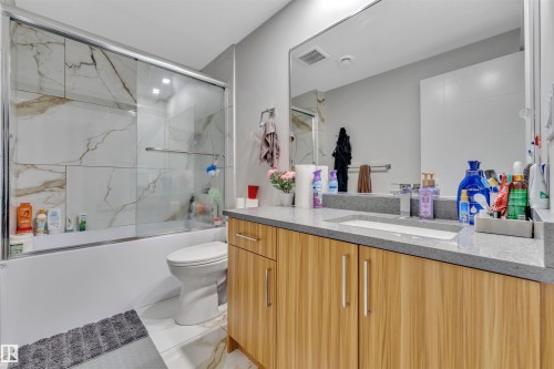 Modern bathroom featuring a wood-finish vanity with an integrated sink, a large mirror, a tiled shower/tub combination with sliding glass doors, and white floor tiles - 1809 18A Avenue, Edmonton, AB - Indoor Photo Showing Bathroom