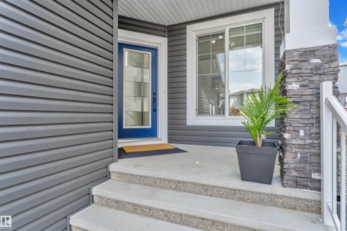 Front entry featuring a blue glass-paneled door, siding exterior, stone-clad pillar, white railing, and concrete steps - 1809 18A Avenue, Edmonton, AB - Outdoor
