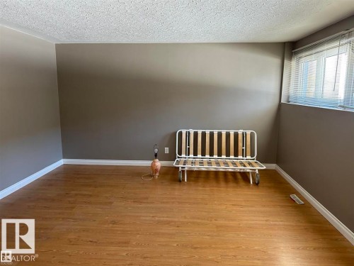 Room featuring wood-finish flooring, neutral wall paint, white baseboards, and a window with horizontal blinds - 2 6920 101 Avenue Nw, Edmonton, AB - Indoor Photo Showing Other Room
