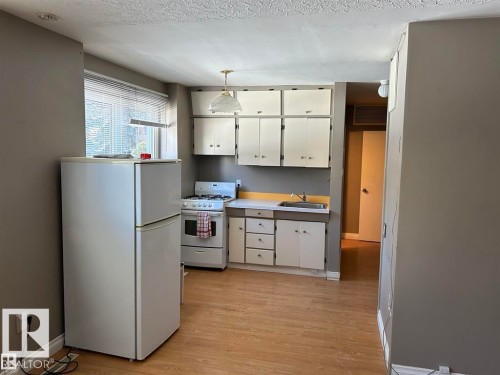 Kitchen area featuring wood-finish flooring, white cabinetry, and a window with blinds - 2 6920 101 Avenue Nw, Edmonton, AB - Indoor Photo Showing Kitchen