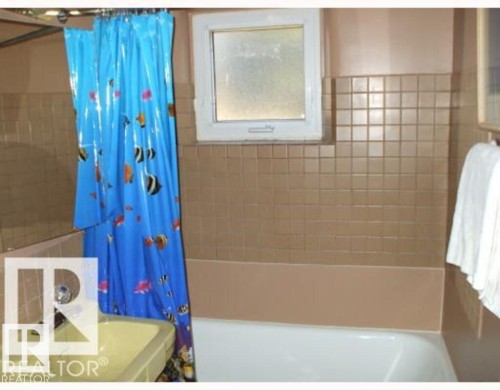Bathroom featuring a white bathtub, light brown wall tiling, and a small rectangular window - 2 6920 101 Avenue Nw, Edmonton, AB - Indoor Photo Showing Bathroom