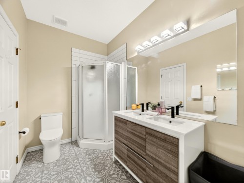 Bathroom featuring a dual-sink vanity with wood-finish cabinetry, a framed mirror, and modern overhead lighting - 7 Oakbay Point(E), St. Albert, AB - Indoor Photo Showing Bathroom