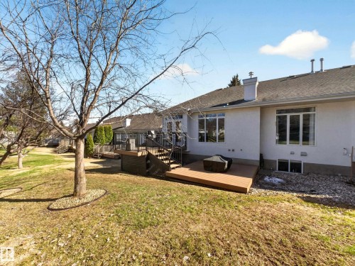 Rear exterior featuring a multi-level composite deck, white stucco siding, and a sloped lawn with mature trees - 7 Oakbay Point(E), St. Albert, AB - Outdoor