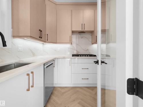 Butlers Kitchen featuring two-tone cabinetry with under-cabinet lighting, a built-in gas range, a stainless steel dishwasher, and a herringbone-pattern wood-finish floor - 2070 Collip Crescent, Edmonton, AB - Indoor Photo Showing Kitchen