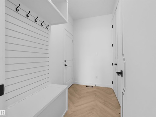 Entryway mudroom featuring herringbone wood-finish flooring, built-in white bench, shiplap-style wall paneling with hooks, overhead shelving, and multiple white doors with matte black hardware - 2070 Collip Crescent, Edmonton, AB - Indoor Photo Showing Other Room
