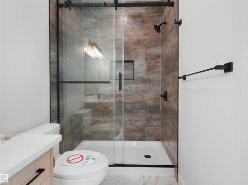 Frameless glass shower enclosure with matte black hardware, featuring rich multi-toned wall tiling and a built-in shower niche - 2070 Collip Crescent, Edmonton, AB - Indoor Photo Showing Bathroom