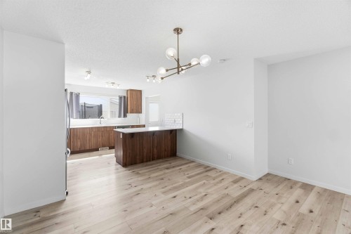 Open-concept living space featuring wood-finish flooring, a modern linear chandelier, and white wall finishes - 22371 93 Avenue, Edmonton, AB - Indoor