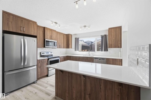 Kitchen featuring wood-finish cabinetry, stainless steel appliances, a center island with a white countertop, and light wood-finish flooring - 22371 93 Avenue, Edmonton, AB - Indoor Photo Showing Kitchen With Upgraded Kitchen