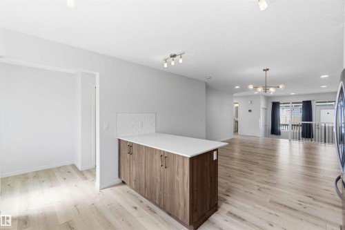 Kitchen island with wood-finish cabinetry and a light-toned countertop, complemented by a textured white tile backsplash - 22371 93 Avenue, Edmonton, AB - Indoor