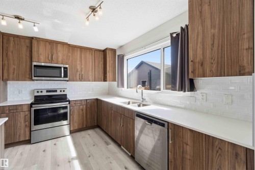 Kitchen featuring wood-finish cabinetry, stainless steel appliances, white subway tile backsplash, and light wood-finish flooring - 22371 93 Avenue, Edmonton, AB - Indoor Photo Showing Kitchen With Double Sink