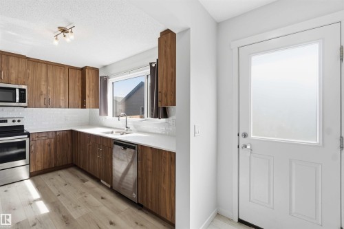 Kitchen featuring wood-finish cabinetry, stainless steel appliances, a white subway tile backsplash, and light wood-finish flooring - 22371 93 Avenue, Edmonton, AB - Indoor Photo Showing Kitchen