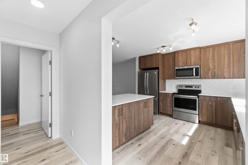 Contemporary kitchen featuring wood-finish cabinetry, stainless steel appliances, white countertops, and a full tile backsplash - 22371 93 Avenue, Edmonton, AB - Indoor Photo Showing Kitchen