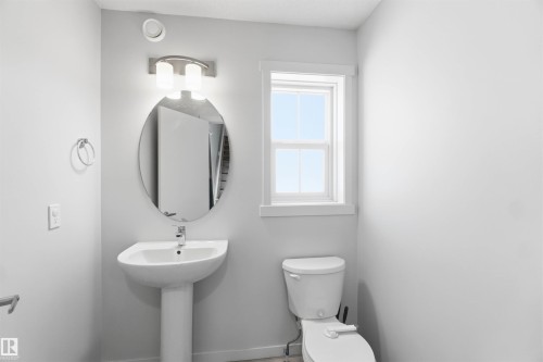 Bathroom featuring a pedestal sink, oval mirror, wall-mounted light fixture, and window with white trim - 22371 93 Avenue, Edmonton, AB - Indoor Photo Showing Bathroom