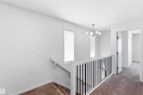 Staircase featuring a contemporary chandelier, white walls, and a white and black railing - 22371 93 Avenue, Edmonton, AB - Indoor Photo Showing Other Room