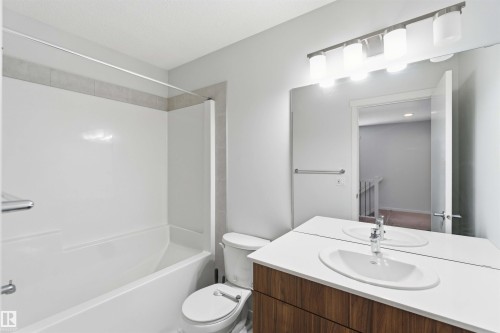 Bathroom featuring a white bathtub and shower surround with a tile accent band, wood-finish vanity with a white countertop and integrated sink, and a large wall-mounted mirror - 22371 93 Avenue, Edmonton, AB - Indoor Photo Showing Bathroom