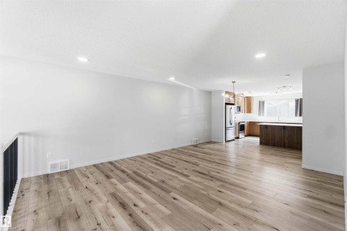 Open-concept living area featuring wood-finish flooring, recessed lighting, and a black metal railing - 22371 93 Avenue, Edmonton, AB - Indoor